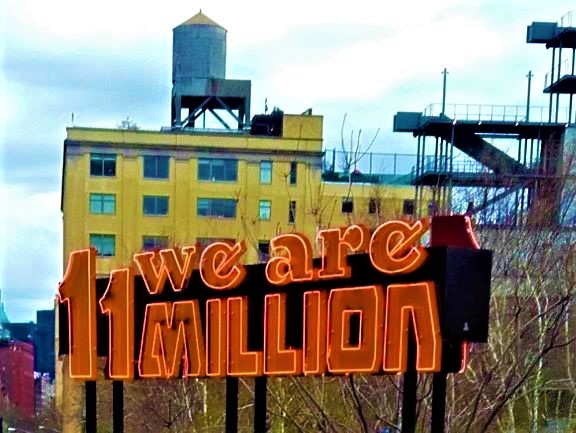 photo of a neon sign which says 'we are 11 million' with industrial building in the background